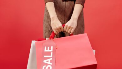 Close-up of a person holding shopping bags with a sale tag on a red background.