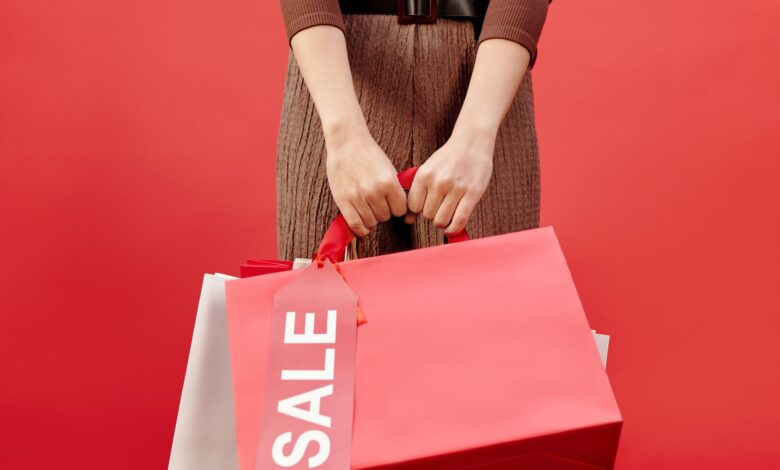 Close-up of a person holding shopping bags with a sale tag on a red background.
