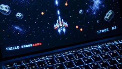 A classic arcade space shooter game displayed on a laptop with illuminated keyboard, showing retro graphics.