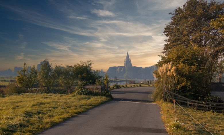 A serene road surrounded by greenery leading to a distant church under a colorful sunset sky.