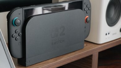 Nintendo console docked among speakers and a monitor on a wooden shelf.