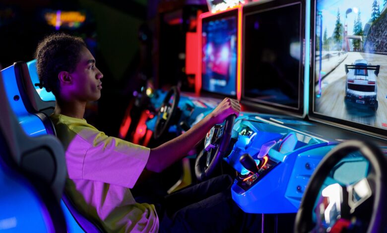 A young man intensely plays a car racing video game at an amusement arcade.