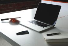 A sleek workspace featuring a laptop, notebook, smartphone, and table tennis paddle on a desk.