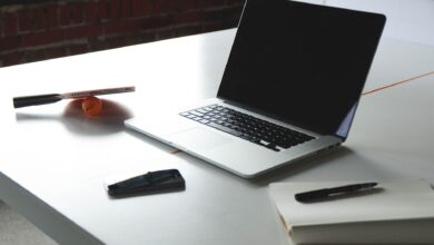 A sleek workspace featuring a laptop, notebook, smartphone, and table tennis paddle on a desk.