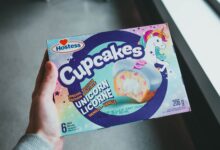 A hand holding a Hostess Unicorn Licorne vanilla cupcakes box with vibrant design.