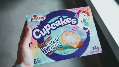 A hand holding a Hostess Unicorn Licorne vanilla cupcakes box with vibrant design.