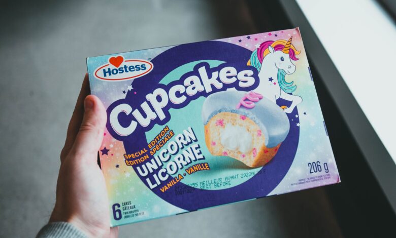 A hand holding a Hostess Unicorn Licorne vanilla cupcakes box with vibrant design.