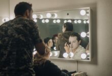 Actors applying makeup backstage in illuminated dressing room before a performance.