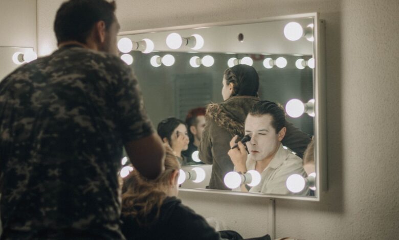 Actors applying makeup backstage in illuminated dressing room before a performance.