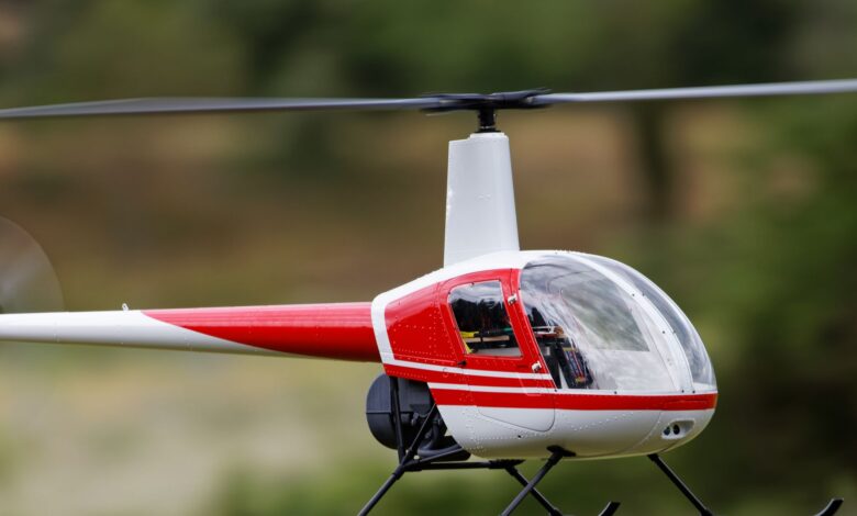 A detailed view of a red remote-controlled helicopter flying outdoors.