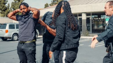 Two law enforcement officers detain a man during a daytime arrest outside a building.