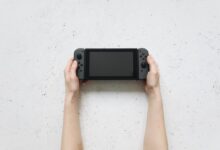 Top view of hands holding a portable gaming console against a textured white background.