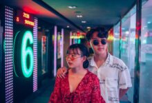 A stylish young couple in a vibrant and modern hallway illuminated by neon lights.