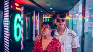 A stylish young couple in a vibrant and modern hallway illuminated by neon lights.