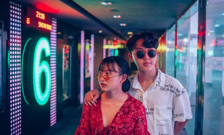 A stylish young couple in a vibrant and modern hallway illuminated by neon lights.