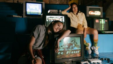 Two women in casual outfits immersed in retro gaming with vintage televisions and game consoles.