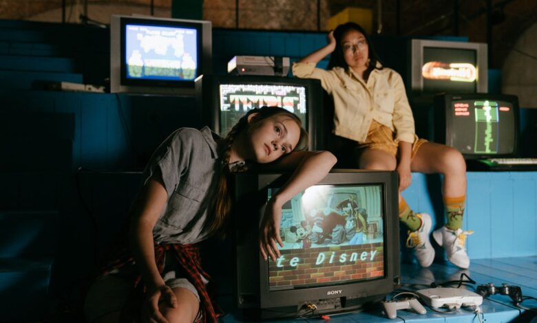 Two women in casual outfits immersed in retro gaming with vintage televisions and game consoles.