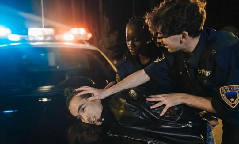 Two police officers arrest a suspect during a nighttime operation with flashing lights.
