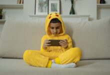 Young boy in a yellow costume playing with a smartphone while sitting on a sofa indoors.