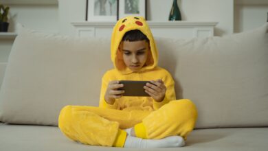 Young boy in a yellow costume playing with a smartphone while sitting on a sofa indoors.