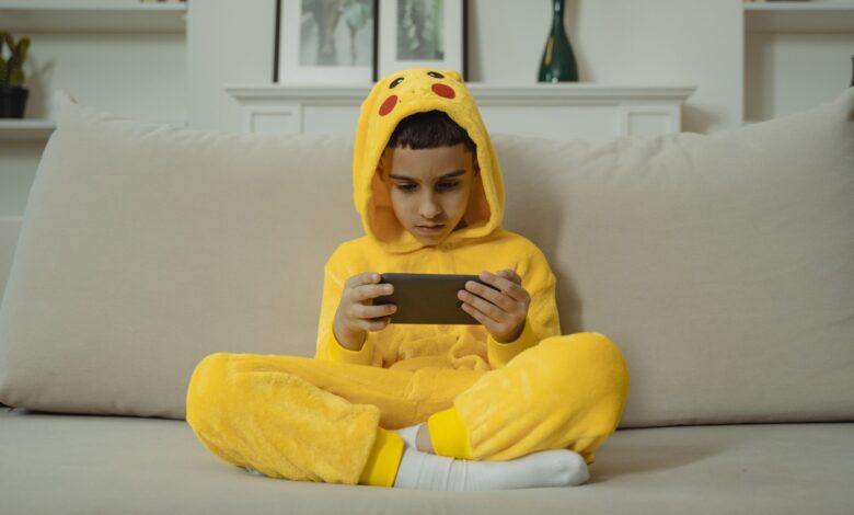 Young boy in a yellow costume playing with a smartphone while sitting on a sofa indoors.