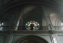 A priest stands at the altar in an ornate church with beautiful arches and stained glass.