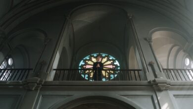A priest stands at the altar in an ornate church with beautiful arches and stained glass.