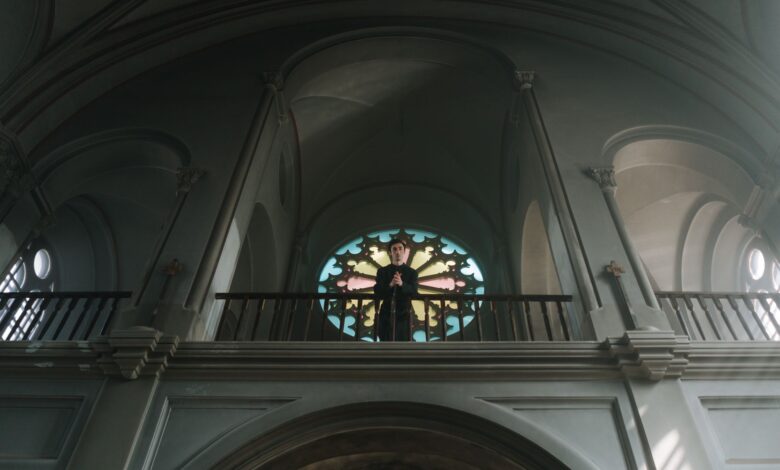 A priest stands at the altar in an ornate church with beautiful arches and stained glass.