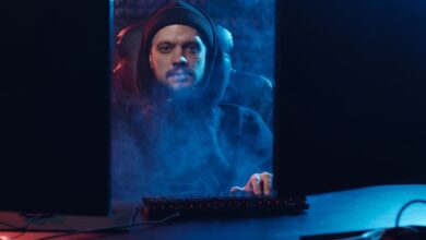 Dramatic scene of an adult man in a hoodie using a computer, surrounded by smoke in a dimly lit room.