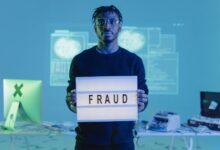 Man holding a 'FRAUD' sign in a tech setting, symbolizing cybersecurity threats.