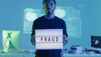 Man holding a 'FRAUD' sign in a tech setting, symbolizing cybersecurity threats.