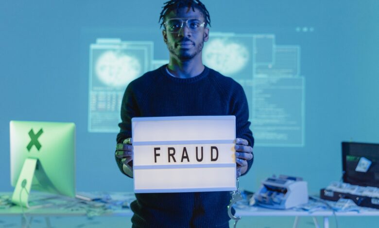 Man holding a 'FRAUD' sign in a tech setting, symbolizing cybersecurity threats.