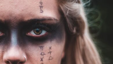 Closeup crop blond with black painted mask on eyes and symbols on skin looking at camera