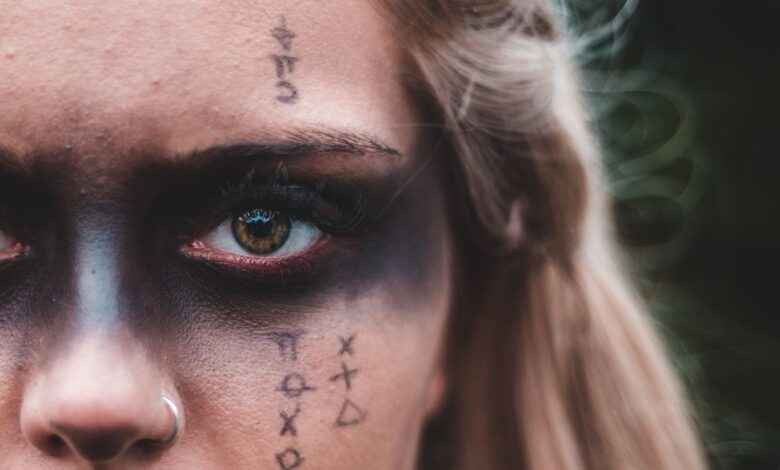 Closeup crop blond with black painted mask on eyes and symbols on skin looking at camera