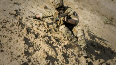 A soldier in full camouflage gear slides down a sandy slope during military training.