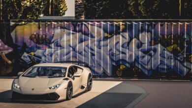 A sleek luxury sports car parked in front of a vibrant graffiti wall under bright daylight.