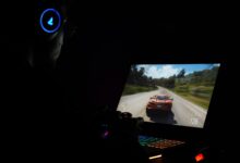 A gamer using a laptop and headphones to play a car racing game in a dark setting.