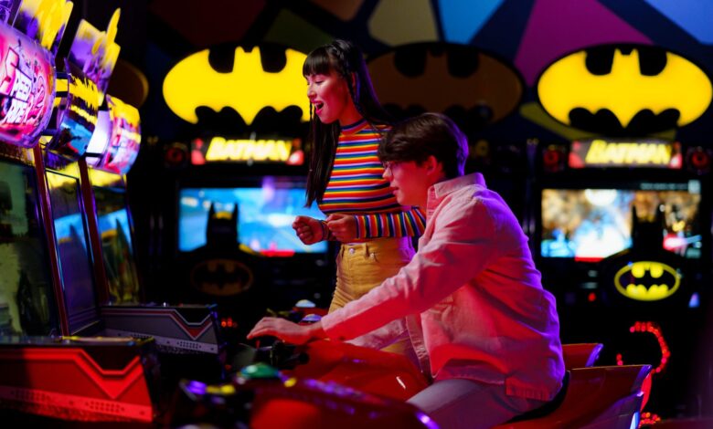 Couple enjoying an arcade gaming night surrounded by neon and Batman decor.