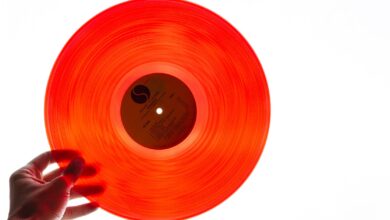 A bright orange vinyl record being held by a hand against a plain white background, showcasing its translucency.