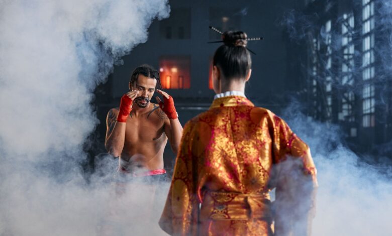Two martial artists in traditional attire face off in a dramatic, smoke-filled arena.