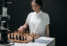A woman plays chess with a robotic arm, illustrating technology and strategy in a modern context.
