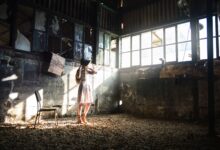Full body of young anonymous female in trendy black hat looking away in sunshine in forgotten building