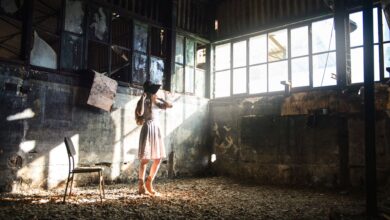 Full body of young anonymous female in trendy black hat looking away in sunshine in forgotten building