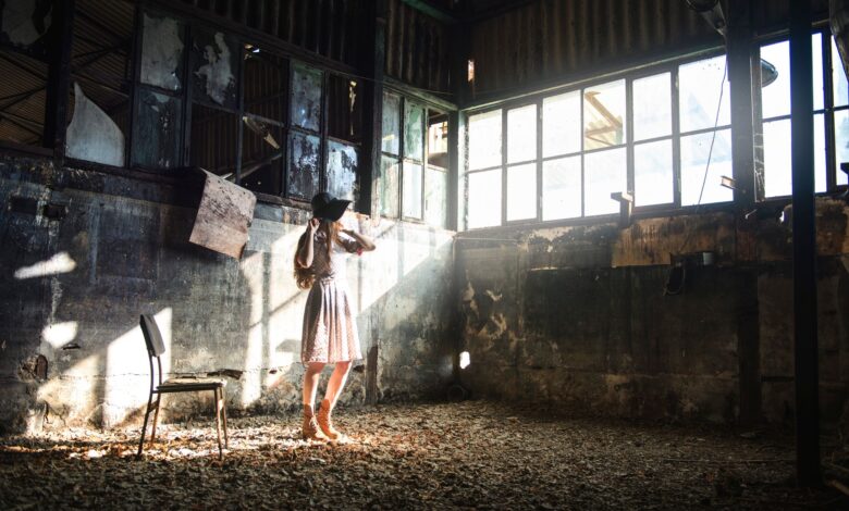 Full body of young anonymous female in trendy black hat looking away in sunshine in forgotten building