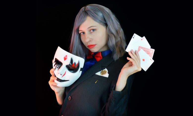 Side view of serious young female casino dealer in classy suit with bow tie holding face mask and cards in hands and looking at camera against black background