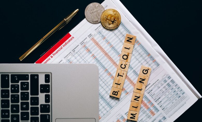 Top view of a laptop, Bitcoin coins, and financial indicators symbolizing Bitcoin mining and investment.