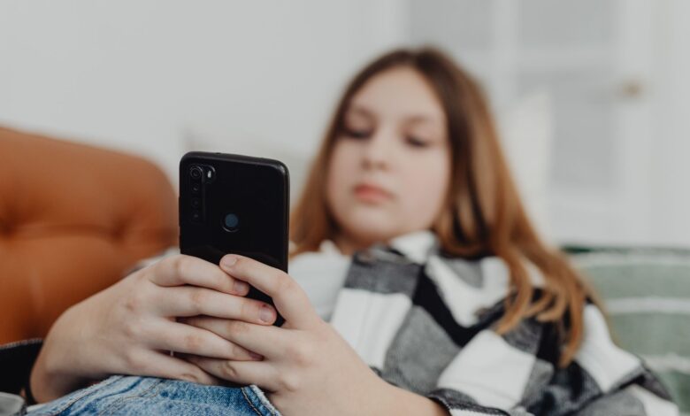 Teenage girl using smartphone while relaxing on a sofa, depicting leisure and connectivity.