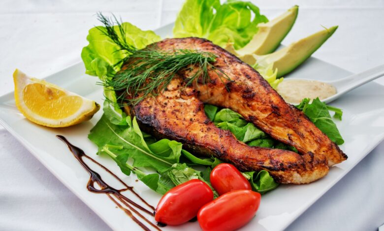 Delicious grilled salmon steak served with avocado, lettuce, cherry tomatoes, and lemon slice on a white plate.