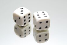A close-up view of two white dice with reflection on a smooth white surface, symbolizing luck and chance.