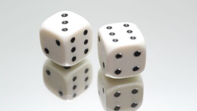 A close-up view of two white dice with reflection on a smooth white surface, symbolizing luck and chance.